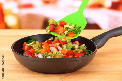 Photo: Vegetable ragout in pan, on wooden table on bright background Vegetable ragout in pan, on wooden table on bright background