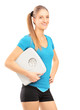 A smiling female athlete holding a weight scale and looking at c