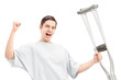 A happy male patient in hospital gown holding crutches and gestu