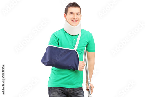 Photo: Full length portrait of a smiling male with broken arm and crutc Full length portrait of a smiling male with broken arm and crutc