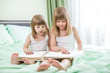 Two little girls reading book sitting on bed