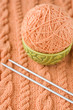 A peach-colored ball of yarn are in dish and needles