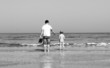 father and son going to swim in the sea.  Black and white photo.