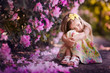 Foto: Adorable toddler girl sitting under blooming tree at sunny sprin Adorable toddler girl sitting under blooming tree at sunny sprin