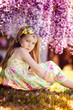 Foto: Adorable toddler girl sitting under blooming wisteria vine at su Adorable toddler girl sitting under blooming wisteria vine at su