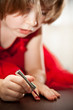 Photo : Little girl in a red dress painted nails with nail polish Little girl in a red dress painted nails with nail polish
