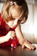 Photo : Little girl in a red dress painted nails with nail polish Little girl in a red dress painted nails with nail polish