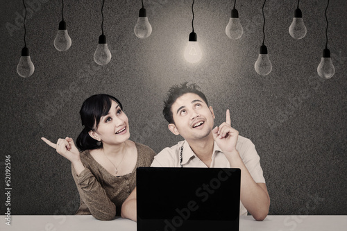 Photo: Couple with laptop looking at lit bulb Couple with laptop looking at lit bulb