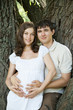 Pregnant wife and her husband outdoors next to trees