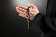Priest holding rosary, on black background