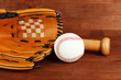 Baseball glove, bat and ball on wooden background