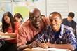 Photo: Teacher Helping Male Pupil Studying At Desk In Classroom Teacher Helping Male Pupil Studying At Desk In Classroom