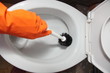 Gloved hand cleaning toilet bowl using brush