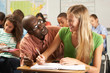 Teacher Helping Female Pupil Studying At Desk In Classroom