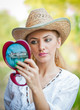 Young blonde woman looking in cosmetic mirror 