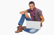 Photo: Happy man sitting on floor using laptop looking at camera Happy man sitting on floor using laptop looking at camera