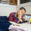 Elementary school age Boy Reading in Bed with Workbook