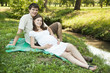 Pregnant wife and her husband lying on green grass