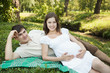 Pregnant wife and her husband lying on green grass
