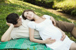 Pregnant wife and her husband lying on green grass