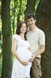 Pregnant wife and her husband in park next to trees