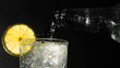 Bottle pouring water into glass with ice and lemon wedge