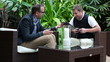 Male friends with smartphone and tablet sitting in garden