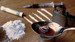 Drug cooking on a spoon surrounded by pile lines and syringe on wooden table
