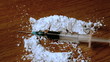 Syringe falling on white substance on wooden table