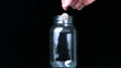 Hand putting two euro coin into glass jar