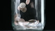 Many coins pouring into glass jar close up