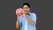 Man shaking piggy bank excitedly on grey background