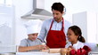 Father watching son stretch pastry with sister