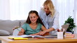 Mother helping her daughter with homework and smiling
