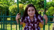 Little girl smiling on a swing in summer park