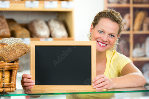 Photo: verkäuferin in bäckerei mit hinweisschild verkäuferin in bäckerei mit hinweisschild