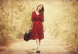 Redhead girl with suitcase at tree's alley.