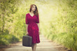 Redhead girl with suitcase at tree's alley.