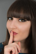 Beautiful young woman gesturing for silence by holding a finger