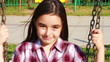 Little girl smiling on a swing in summer park