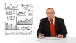 Businessman sitting at desk with diagrams and holding a mobileph