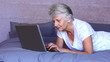 Woman lying on bed using laptop