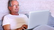 Elderly man using laptop in bed