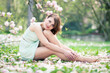 Beautiful young woman sitting under a magnolia tree in bloom