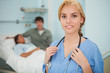 Blonde nurse looking at camera next to a patient