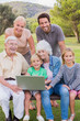 Portrait of happy multi-generation family in the park using laptop