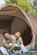 Father helping son to read at the campsite while mother is watching