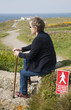 Woman with walking stick sitting by red notice