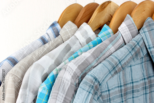 Photo: Shirts with ties on wooden hangers on light background Shirts with ties on wooden hangers on light background