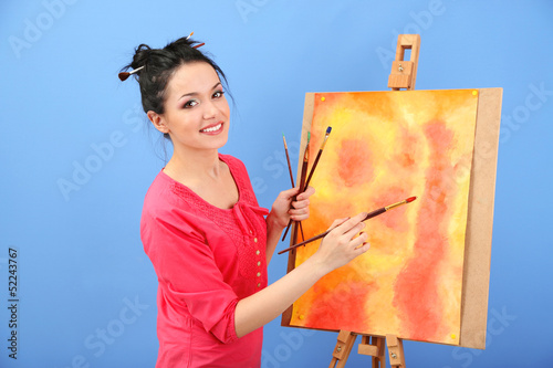 Photo: Beautiful young woman painter at work, on color background Beautiful young woman painter at work, on color background